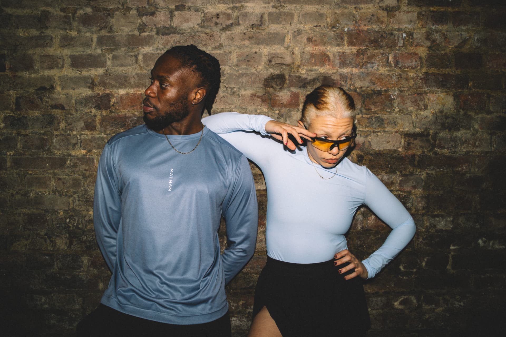Two people wearing MATHAN activewear against a brick wall
